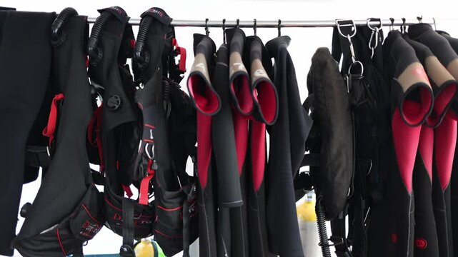 Scuba diving gear hanging wetsuits and BCDs ready for adventure vibrant red and black tones organized setup oxygen tanks below clean and professional look for underwater exploration