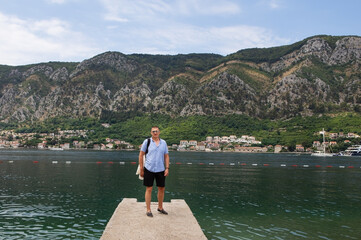 A man enjoys a scenic view of a bay and mountains, standing on a small pier