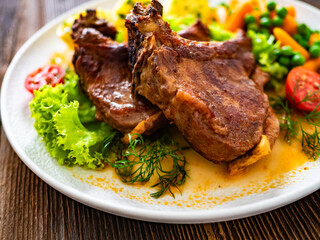 Baked veal chops, boiled potatoes, green peas and carrots on wooden table