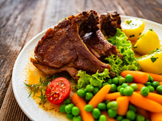 Baked veal chops, boiled potatoes, green peas and carrots on wooden table