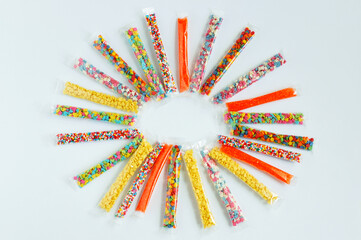 Multi-colored confectionery sprinkles in individual transparent packaging are laid out in the shape...