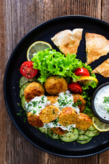 Fried meatballs with tzatziki sauce and pita bread on wooden table. Greek style food