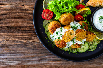 Fried meatballs with tzatziki sauce and pita bread on wooden table. Greek style food