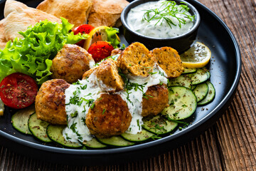 Fried meatballs with tzatziki sauce and pita bread on wooden table. Greek style food