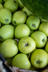 A close-up, top-down view of a bountiful display of vibrant green apples, likely Granny Smiths, partially obscured by a watermelon, highlighting fresh produce at a market