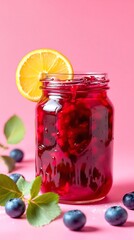 Glass jar filled with red jam and a lemon slice on a pink background with blueberries around it