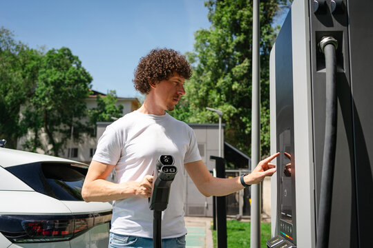 Man charging an electric car in an urban environment