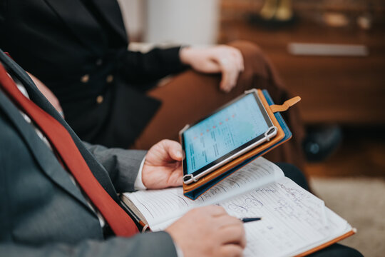 Close-up of business team members working with a tablet and notebook during a discussion, focusing on collaboration and the utilization of digital tools for strategic planning and problem-solving.