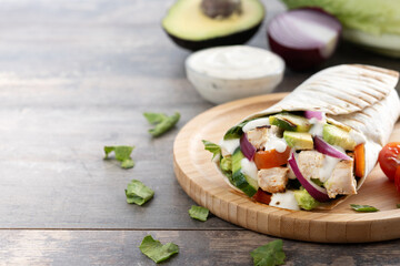 A delicious grilled chicken wrap with vegetables and avocado on wooden table. Copy space