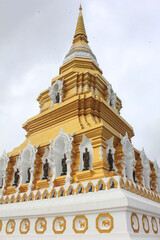 Obraz premium Golden Buddhist Pagoda in Thailand. A golden stupa decorated with Buddha statues and ornate carvings, representing Thai Buddhist architecture under cloudy sky.