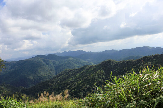 Rolling Hills Under Bright Clouds, Khao Chang Phueak. A panoramic view of rolling green hills under a sky filled with scattered clouds, with tall grass in the foreground.