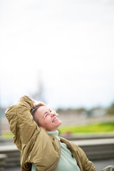 Relaxed woman with short blond hair smiling with eyes closed while leaning back outdoors