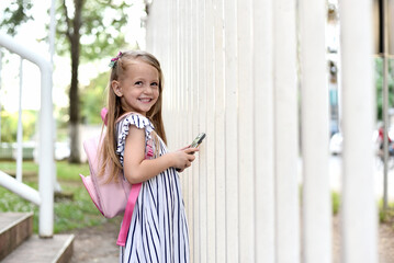 Cute school girl with backpack using smartphone
