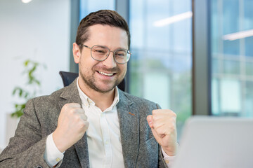 An enthusiastic businessman celebrates a win, showing joy with clenched fists and a big smile.
