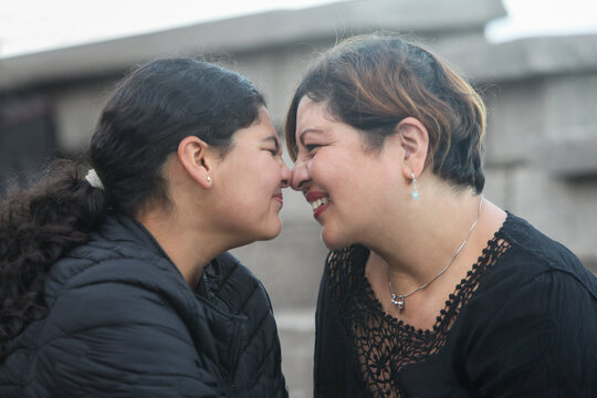closeup portrait of mid adult hispanic mother with her teenage daughter nose to nose facing each other outdoors smiling