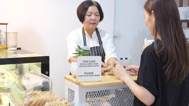 A deaf person is employed as a staff at coffee shop, pin a deaf staff sign on apron, using sign language to communicate with customers to take orders at the counter.