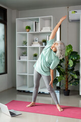 Wellness and Fitness. Senior woman stretching during online yoga class at home.