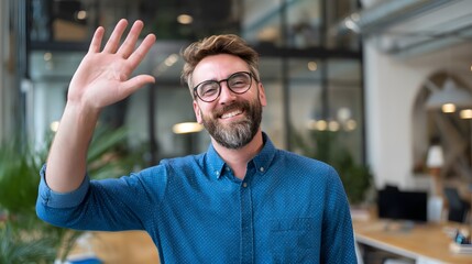 Cheerful man smiling and waving, conveying warm greeting in modern office environment with bright interior