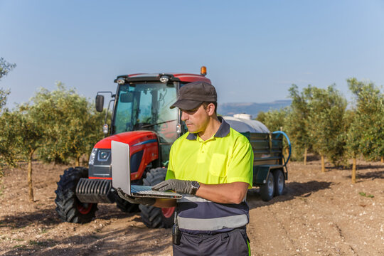 Man operating laptop in olive field in Andalucia, agricultural worker with tractor background
