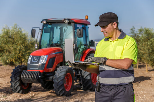 Farm worker using a tablet while operating a tractor in an olive grove