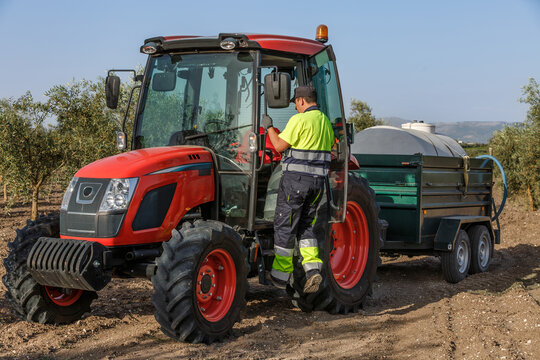 Tractor operator preparing for work in olive orchard under clear blue sky