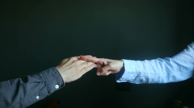 Business colleagues engaged in playful rock paper scissors game, showcasing competitive spirit through dynamic hand gestures and strategic workplace interaction against neutral dark gray backdrop