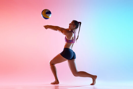 Side view of female player hitting volleyball in mid-motion with vibrant neon light against gradient studio background. Concept of impact, core power, sport dynamics, and controlled technique.