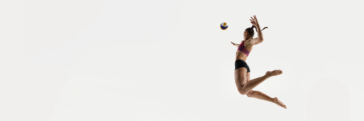 Banner. Side view of jumping woman about to hit volleyball against white studio background with negative space to insert text. Copy space. Concept of sport events, championship, timing, serve position