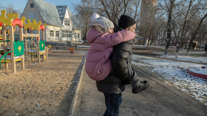 Grandfather playing with her granddaughter on the playground in the park in winter