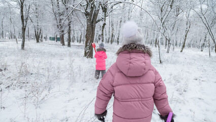 Two little girls in colorful clothes play outdoors during a snowfall.