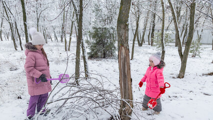 Two little girls in colorful clothes play outdoors during a snowfall.