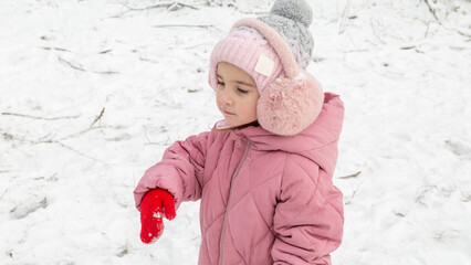 Cheerful positive child girl wearing a outerwear smiling walking through a snowy countryside forest