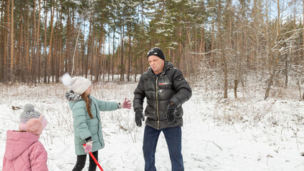 Little girls play with snow with her grandfather in winter forest