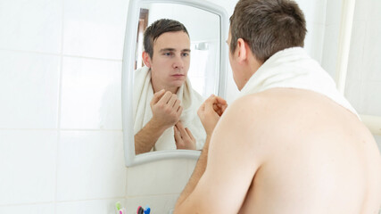 Young handsome man is wiping his face using a towel while looking into the mirror in bathroom.