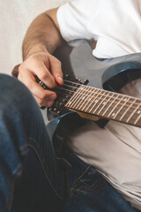 Man's hands playing electric guitar, close up at home
