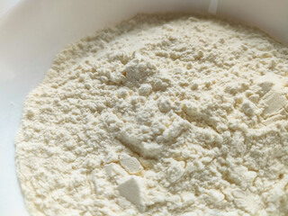 White flour in a clean white bowl on a white background. Minimalist cooking ingredient for baking and culinary use.