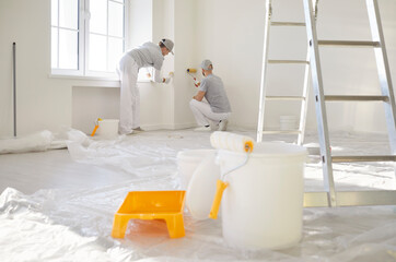 Paint roller, buckets, tray and ladder symbolizing renovation process in progress with two painters...