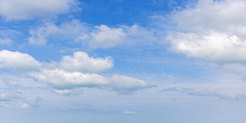 Light and fluffy white cumulus clouds scatter across a bright blue sky