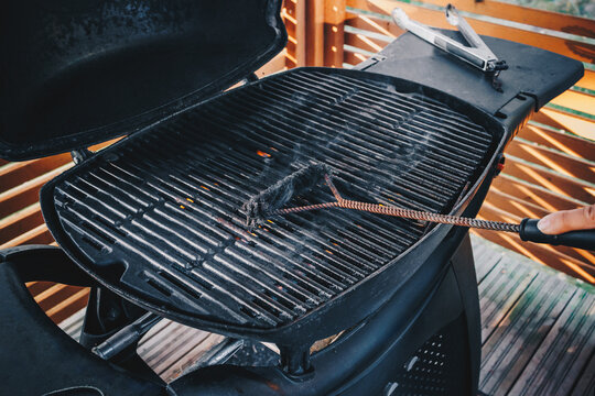 Cleaning outdoor barbecue grill. Close-up of a person cleaning a bbq grill with a wire brush with rising smoke.
