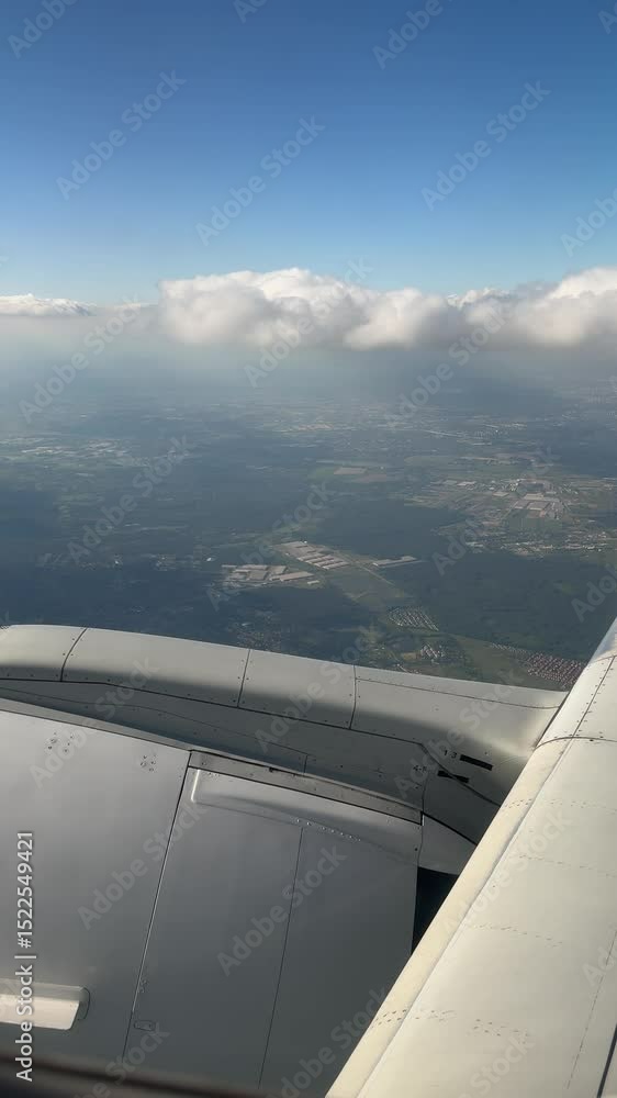 Poster view from airplane window over green fields and scattered settlements under cloudy blue sky in polan