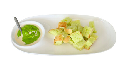 Green pandan-flavored bread cubes served on a white plate with a bowl of Thai-style custard dip made from coconut milk and pandan.
