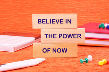 Finance and business concept. Text BELIEVE IN THE POWER OF NOW made of wooden blocks on an orange...
