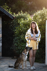 Obraz premium A woman laughs beside her calm dog in a sunny backyard with a stone house