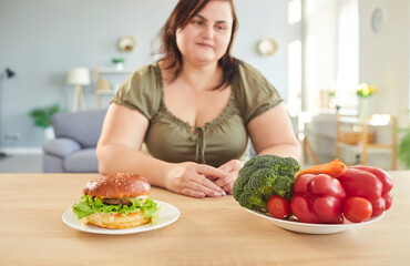 Portrait of fat young overweight plus size woman sitting at table at home and looking at a plate...