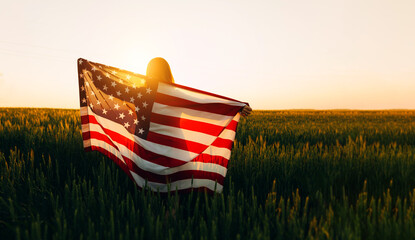 Young woman with American flag in a wheat field at sunset. 4th of July. Patriotic holiday, american...