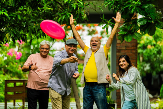 Elderly Indian friends playing frisbee and having fun during outdoor garden meetup