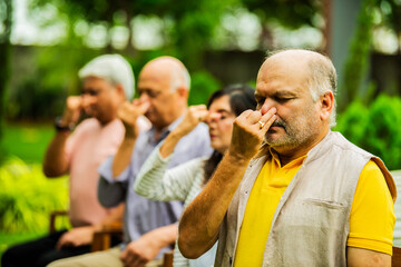 Indian seniors doing Pranayama in group while seated outdoors in garden with closed eyes
