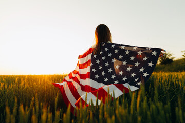 Young woman with American flag in a wheat field at sunset. 4th of July. Patriotic holiday, american...