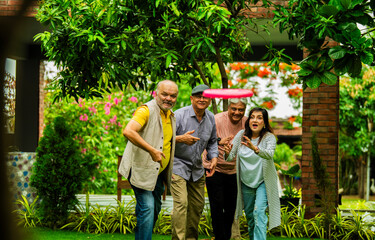 Elderly Indian friends playing frisbee and having fun during outdoor garden meetup