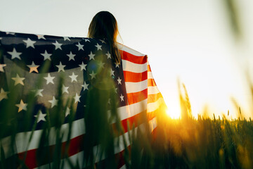 Young woman with American flag in a wheat field at sunset. 4th of July. Patriotic holiday, american...